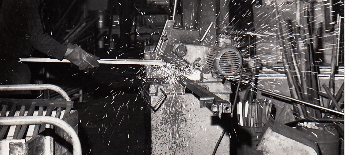 Czarno-białe zdjęcie pracownika obrabiającego półkę w latach 70. XX wieku
	                        