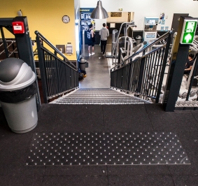 Widok ze szczytu schodów ERP w hali sportowej z okładziną bezpieczeństwa i oznakowaniem wyjścia awaryjnego
			