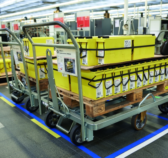 Zmotoryzowane wózki używane do przenoszenia części na paletach w fabryce
		                    